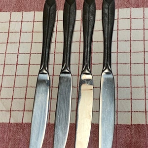 Può includere: Quattro coltelli da tavola in argento con manici neri. I coltelli hanno un design semplice ed elegante.