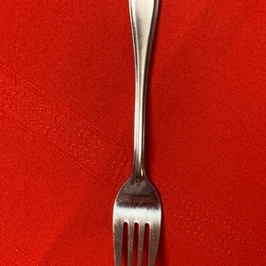 May include: A stainless steel fork with four tines, set against a vibrant red background. The fork's handle has a rounded, slightly curved design. The tines are evenly spaced and pointed.