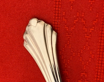 May include: Close-up of the top of a silver spoon with a fluted design.
