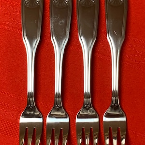 May include: Four silver forks with ornate handles and three prongs. The forks are arranged in a row on a red surface.