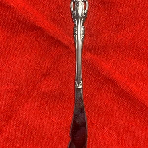 May include: A silver butter knife with an ornate handle. The knife has a slightly curved blade and a decorative design on the handle.