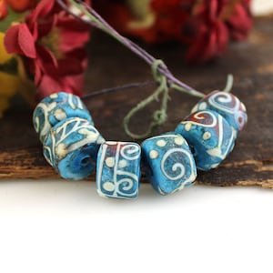 May include: A strand of blue and white ceramic beads with intricate white designs. The beads are cylindrical and have a slightly rounded shape. The beads are strung on a thin cord.