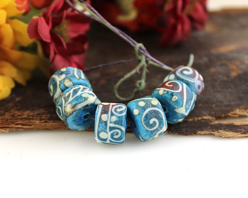 May include: A strand of blue and white ceramic beads with intricate white designs. The beads are cylindrical and have a slightly rounded shape. The beads are strung on a thin cord.
