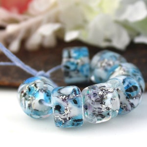 May include: A strand of blue and white glass beads with a silver glitter effect. The beads are round and have a mottled appearance.