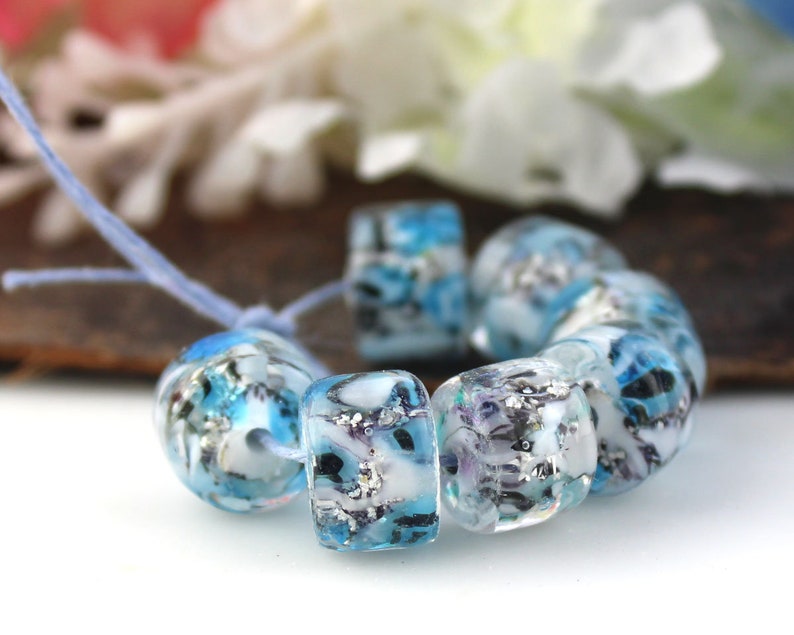 May include: A strand of blue and white glass beads with a silver glitter effect. The beads are round and have a mottled appearance.