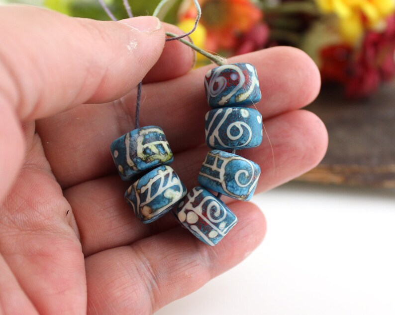 May include: A strand of blue and white ceramic beads with intricate patterns. The beads are strung on a thin cord and are approximately 1 inch in diameter.