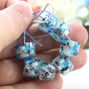 May include: A strand of blue and white glass beads with silver flecks. The beads are square shaped and have a translucent appearance.