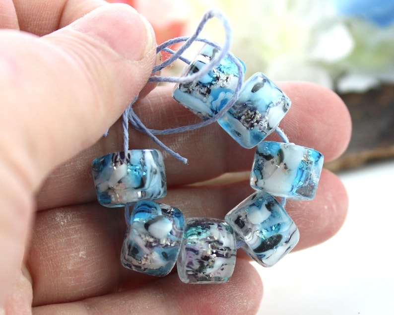 May include: A strand of blue and white glass beads with silver flecks. The beads are square shaped and have a translucent appearance.