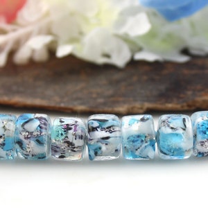 May include: A strand of eight blue and white glass beads with silver flecks. The beads are cylindrical and have a marbled appearance.
