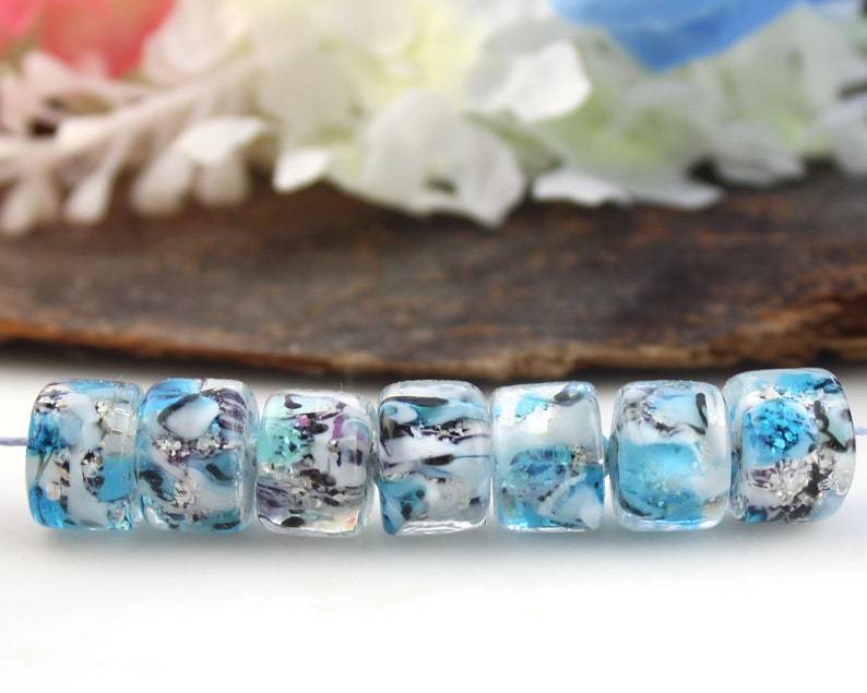 May include: A strand of eight blue and white glass beads with silver flecks. The beads are cylindrical and have a marbled appearance.