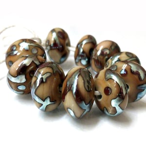 May include: A collection of artisan beads in shades of brown, tan, and iridescent blue. The beads have a glossy finish and a unique, swirling pattern. They are strung together with a white cord, perfect for jewelry making or crafting projects.