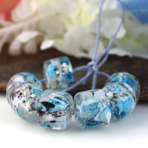 May include: A strand of blue and white glass beads with a marbled effect. The beads are strung on a blue cord.
