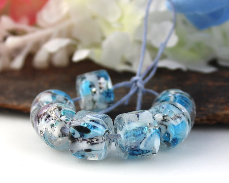 May include: A strand of blue and white glass beads with a marbled effect. The beads are strung on a blue cord.