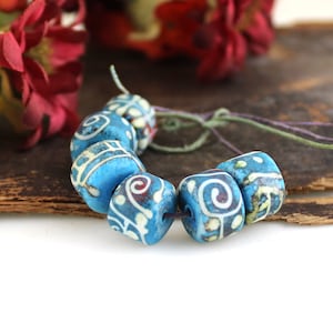 May include: A strand of blue and white ceramic beads with intricate patterns. The beads are strung on a thin cord and have a slightly worn, vintage look.