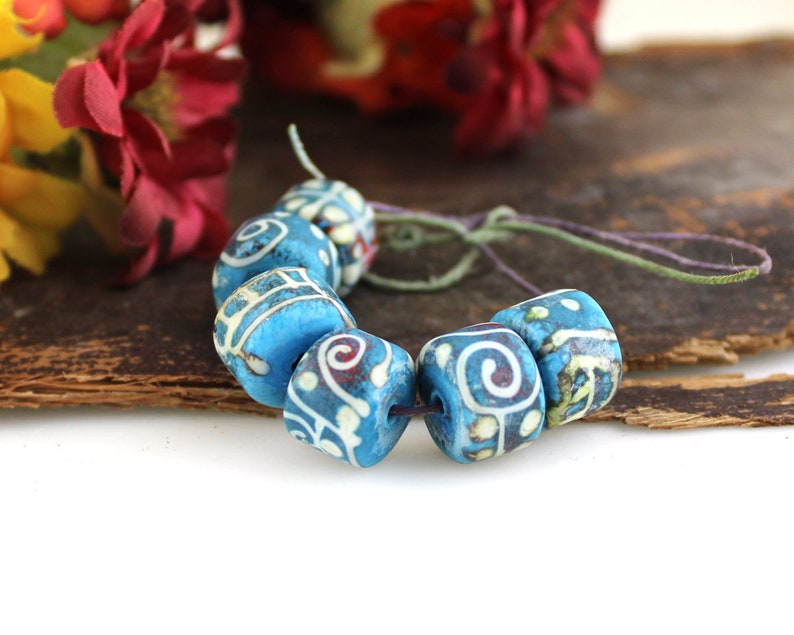 May include: A strand of blue and white ceramic beads with intricate patterns. The beads are strung on a thin cord and have a slightly worn, vintage look.