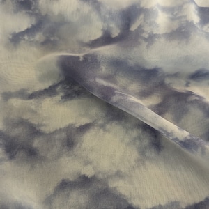 May include: A white fabric with a blue cloud pattern. The fabric is creased and has a soft, flowing texture.