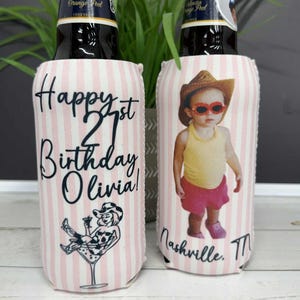 May include: Two beer can coolers with a pink and white striped pattern. One cooler says "Happy 21st Birthday Olivia!" with a cartoon image. The other cooler has a photo of a baby wearing a cowboy hat and sunglasses. The text "Nashville, TN" is below the photo.