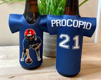 May include: Two beer bottle coolers in the shape of football jerseys. One cooler features a photo of a football player, the other has the name "PROCOPIO" and the number "21" in white on a navy blue background.