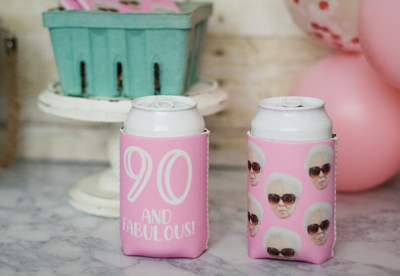 May include: Two pink can coolers. One cooler has the number 90 and the words "and fabulous!" printed on it. The other cooler has a pattern of a woman wearing sunglasses.