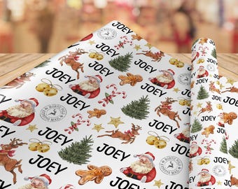 May include: White wrapping paper featuring a repeating pattern of the name JOEY in black text, alongside illustrations of Santa Claus, reindeer, gingerbread men, candy canes, Christmas trees, gold bells, stars, and North Pole postmarks.