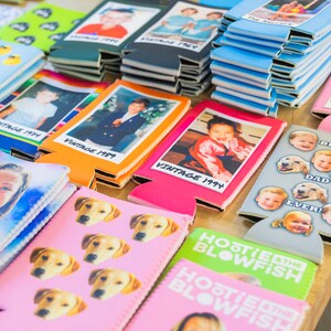 Puede incluir: Una colecci&oacute;n de enfriadores de latas coloridos con varias im&aacute;genes y texto. Algunos enfriadores presentan fotos de ni&ntilde;os, mientras que otros tienen im&aacute;genes de perros o texto como "Hootsie Blowfish".