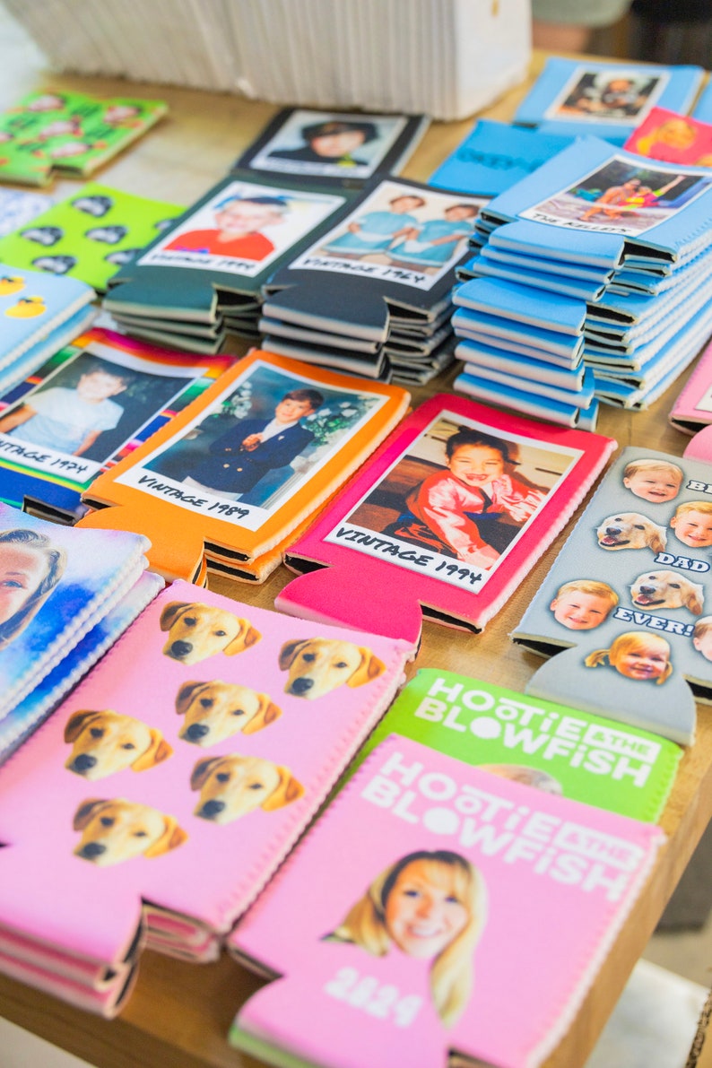Puede incluir: Una colecci&oacute;n de enfriadores de latas coloridos con varias im&aacute;genes y texto. Algunos enfriadores presentan fotos de ni&ntilde;os, mientras que otros tienen im&aacute;genes de perros o texto como "Hootsie Blowfish".