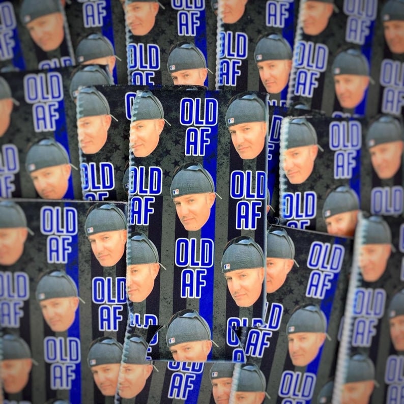 May include: A close-up of a stack of blue and black can coolers with the text "Old AF" printed on them. The coolers feature a repeated pattern of the text and a man's face.
