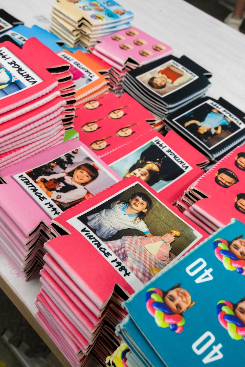 May include: A collection of foam beverage insulators in various colors including pink, black, and teal. The insulators feature printed photographs of children, people, and balloon art, with text such as Vintage 1984, Vintage 1991, and the number 40.