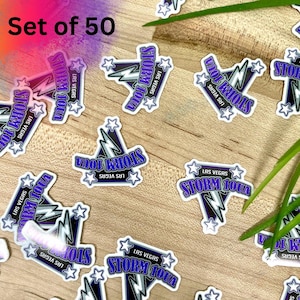 May include: A collection of stickers with a white border, featuring the text "LAS VEGAS STORM 10UA" in a stylized font. The design includes a lightning bolt and stars in shades of blue and purple. The words "Set of 50" are in the top left corner.