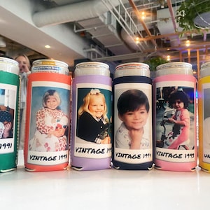 May include: A row of colorful foam beverage can coolers, each featuring a printed vintage photograph of a child and the text VINTAGE followed by a year. The coolers are green, orange, lavender, navy blue, pink, and yellow, holding metal cans.