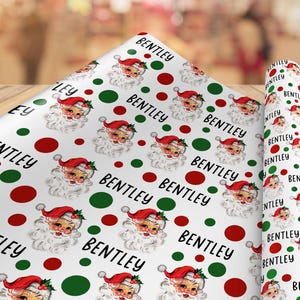 May include: White wrapping paper featuring a repeating pattern of vintage-style Santa Claus faces, red and green polka dots, and the name Bentley printed in a black sans-serif font throughout the design on a continuous roll of paper.