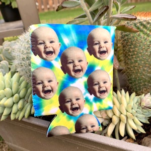 May include: A blue and yellow tie-dye can cooler with multiple images of a baby smiling. The cooler is made of neoprene and has a sewn seam around the edge.
