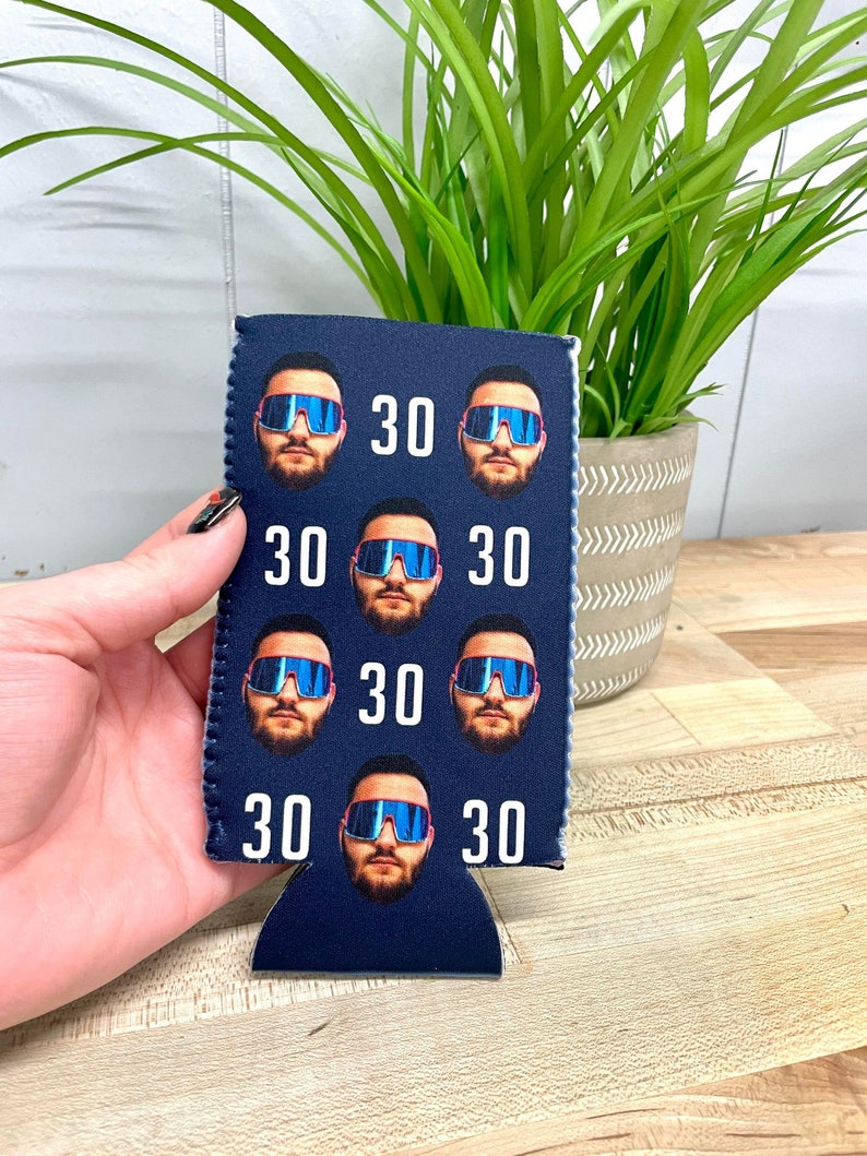 May include: A blue neoprene can cooler with a repeated pattern of a man's face wearing sunglasses and the number 30.