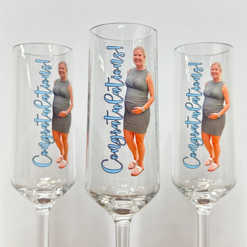 May include: Three clear glass champagne flutes with a personalized design. Each flute features a photo of a pregnant woman and the text "Congratulations!" in blue lettering.