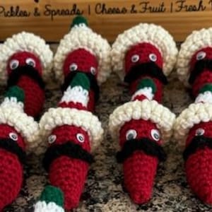May include: A collection of 14 crocheted red chili peppers wearing white sombreros with black mustaches and googly eyes.