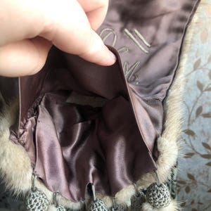 May include: A brown fur stole with a satin lining and a grey crocheted tassel trim. The lining has the text "21 M." embroidered on it.