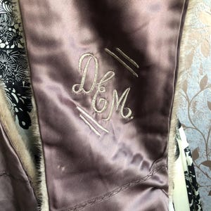 May include: A close-up of a mauve satin fabric with a white embroidered monogram that reads "D&M".