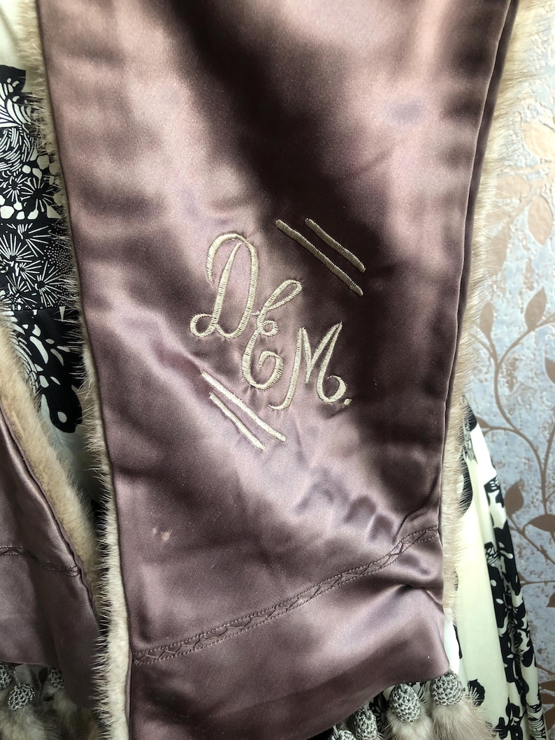May include: A close-up of a mauve satin fabric with a white embroidered monogram that reads "D&M".