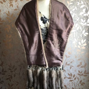 May include: A brown fur stole with a satin lining and a fringe of fur tails. The stole is embroidered with the initials "D.M."