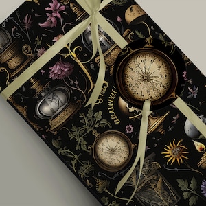 May include: A black and gold gift wrap with a repeating pattern of vintage compasses, lanterns, and flowers. The ribbon is a light beige colour.