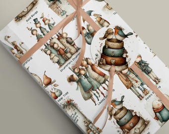 May include: A rectangular gift wrapped in white paper featuring a repeating watercolour illustration of characters and text including Gold Rings, Drummers Drumming, Pear Tree, and Ladies Dancing, tied with a light pink ribbon and a circular gift tag.