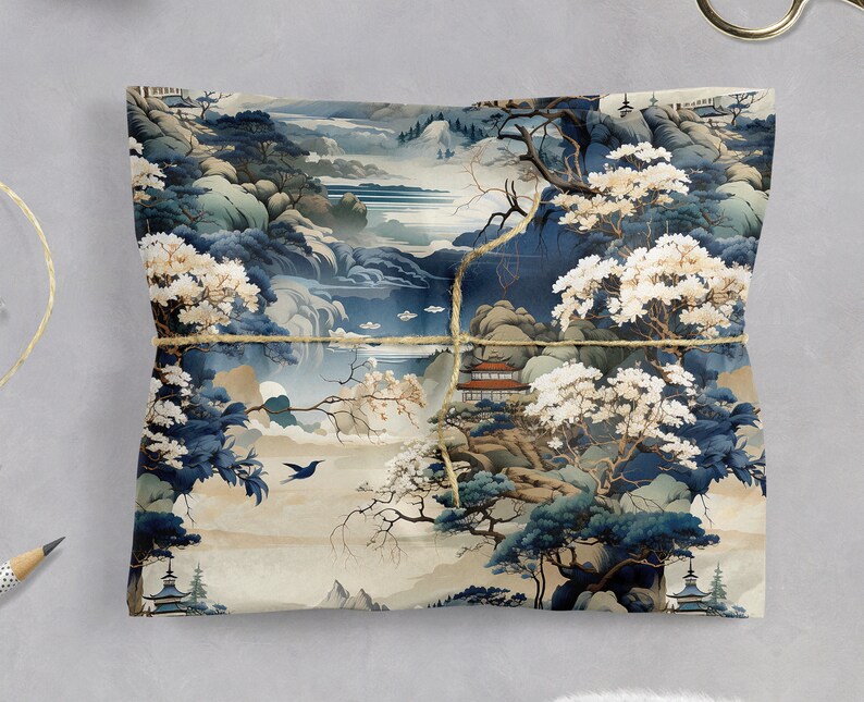 May include: A square sheet of wrapping paper featuring a detailed landscape illustration in shades of blue, cream, and white. The design depicts mountains, trees with white blossoms, a small building with a red roof, and a bird, tied with twine.