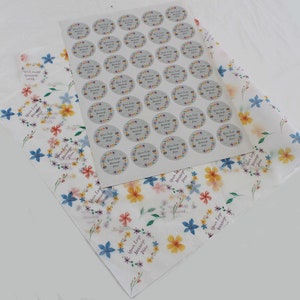 May include: A sheet of white tissue paper with a floral pattern in shades of blue, yellow, and pink. A sheet of stickers with 49 round stickers with a floral wreath design and the text "Your Logo Message Here" is on top of the tissue paper.