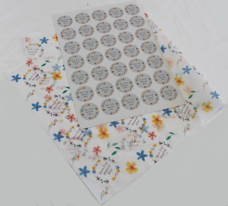 May include: A sheet of white tissue paper with a floral pattern in shades of blue, yellow, and pink. A sheet of stickers with 49 round stickers with a floral wreath design and the text "Your Logo Message Here" is on top of the tissue paper.