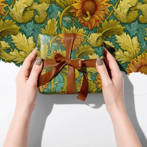 Puede incluir: Una caja de regalo envuelta con un estampado floral de girasoles y hojas en tonos amarillos, verdes y turquesas. La caja est&aacute; atada con una cinta y un lazo marrones. El fondo es un dise&ntilde;o floral a juego.