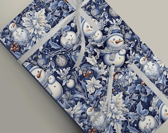 May include: A rectangular gift box wrapped in dark blue and white paper featuring a repeating pattern of snowmen, Christmas ornaments, holly leaves, and poinsettia flowers, tied with a white ribbon that crosses over the top surface.