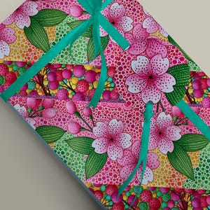 May include: A gift box wrapped in pink floral patterned paper with a teal ribbon. The paper features pink cherry blossoms, green leaves, and red berries on a dotted background. The ribbon is tied in a bow.