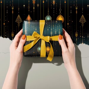 Puede incluir: Una caja de regalo envuelta en papel azul oscuro con un patr&oacute;n geom&eacute;trico dorado y una cinta amarilla. La caja est&aacute; siendo sostenida por dos manos con esmalte de u&ntilde;as naranja.