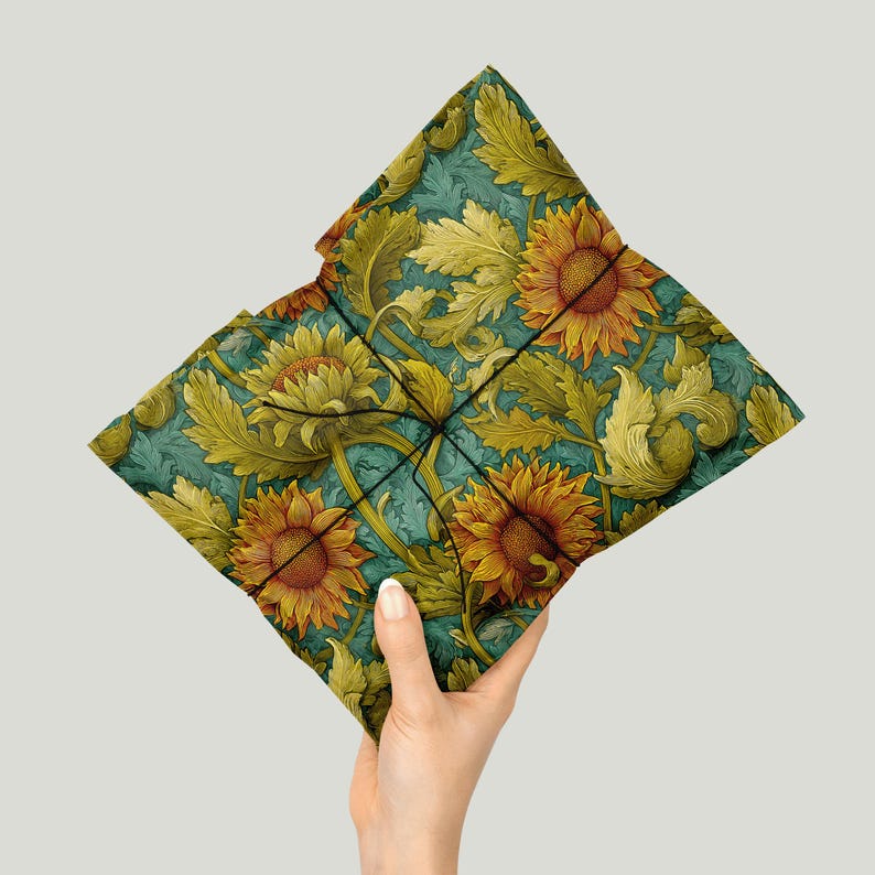 Puede incluir: Un coj&iacute;n decorativo con un estampado floral de girasoles. El coj&iacute;n presenta grandes girasoles en tonos naranja y amarillo, sobre un fondo turquesa con hojas verdes. El coj&iacute;n est&aacute; sostenido por una mano.