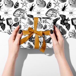 Monochrome witch craft artwork on wrapping paper, a box being held in two hands with an orange ribbon